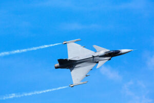 Modern jet fighter flying against a blue sky. White smoke trail.