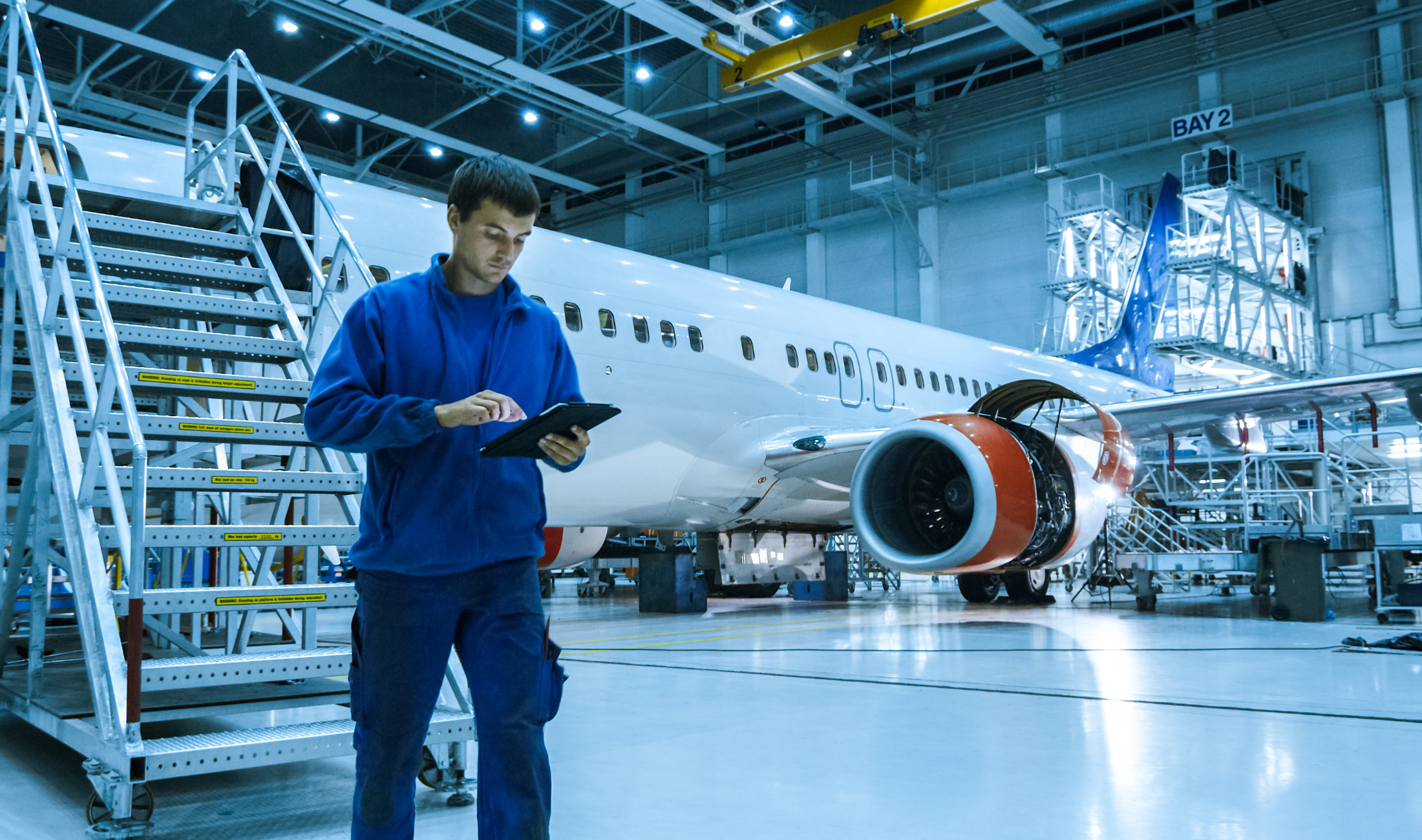 Man standing with tablet in an airplane hangar next to an airplane.